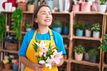 Middle age woman florist holding bouquet of flowers at flower shop