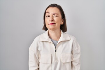 Middle age hispanic woman standing over isolated background winking looking at the camera with sexy expression, cheerful and happy face.