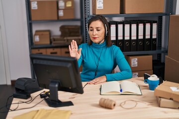 Middle age hispanic woman working at small business ecommerce on customer support with open hand doing stop sign with serious and confident expression, defense gesture