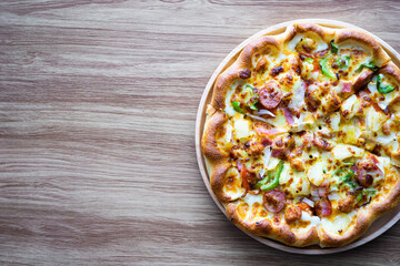 Supreme or deluxe pizza on round plate and wood background, right on frame, copy space on left