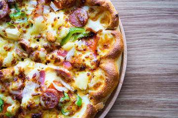 Close and haft of supreme or deluxe pizza on round plate and wood background, left on frame, copy space on right