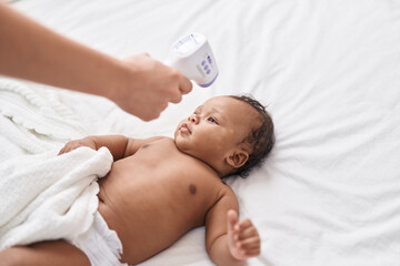 Obraz na płótnie Canvas African american baby measuring temperature at bedroom