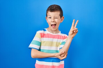 Young caucasian kid standing over blue background smiling with happy face winking at the camera...