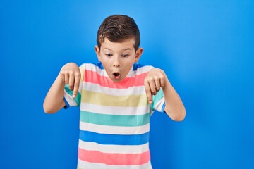 Young caucasian kid standing over blue background pointing down with fingers showing advertisement,...