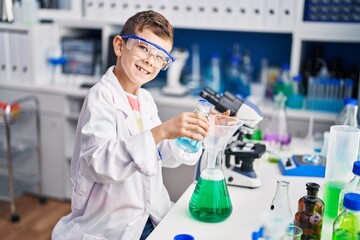 Blond child wearing scientist uniform measuring liquid at laboratory