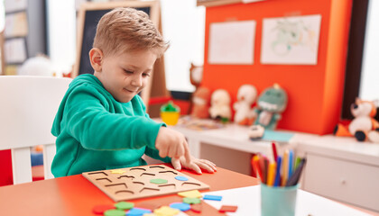 Adorable caucasian boy playing with maths puzzle game sitting on table at kindergarten