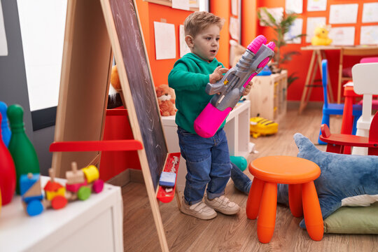 Adorable caucasian boy standing with relaxed expression playing with pistol toy at kindergarten