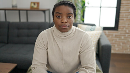 African american woman sitting on sofa with serious expression at home