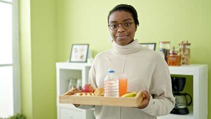 African american woman smiling confident holding breakfast tray at dinning room