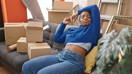 Fototapeta na wymiar African american woman relaxed with hands on head sitting on sofa at new home
