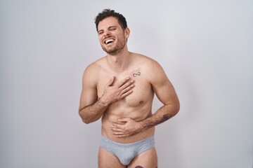 Fototapeta na wymiar Young hispanic man standing shirtless wearing underware smiling and laughing hard out loud because funny crazy joke with hands on body.