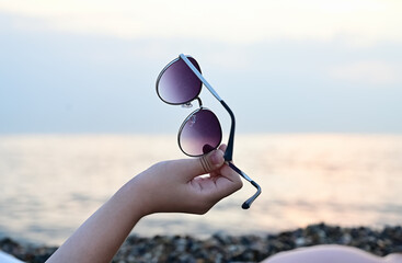 Fototapeta na wymiar sunglasses in the hands of a woman on the background of the seashore
