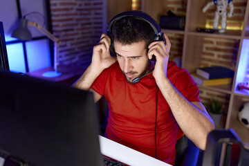 Young hispanic man streamers sitting on table with relaxed expression at gaming room