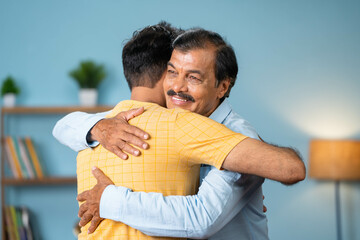 Happy Indian thankful adult son hugging or embracing to senior father at home - concept of emotional love, gratefulness and fathers day greeting