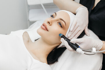 View of doctor cosmetologist doing anti aging procedure in cosmetology office. Satisfied woman in...