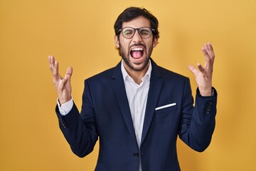 Handsome latin man standing over yellow background celebrating mad and crazy for success with arms raised and closed eyes screaming excited. winner concept