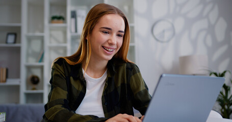 Portrait happy woman sitting at open laptop screen after work and looking at camera, smiling. Smiling girl freelancer using laptop chatting with friends or customer social media.