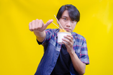 Attractive young Asian man holding noodles in the cup of paper. A young Asian man enjoys instan noodles with an expression of satisfaction.