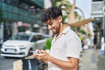 Young arab man smiling confident watching video on smartphone at street