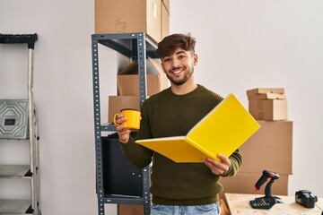 Young arab man ecommerce business worker reading notebook drinking coffee at office