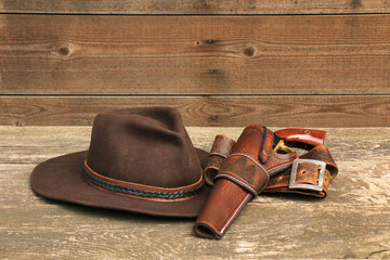 A black powder revolver in a leather holster with a leather belt next to a felt cowboy hat, on the...
