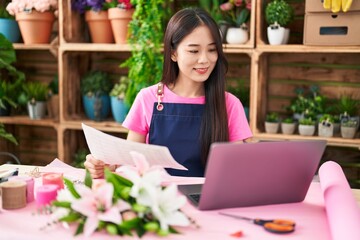Young chinese woman florist using laptop reading document at flower shop