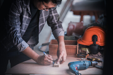 Skilled carpenter cutting a piece of wood in his woodwork workshop, using a hand saw, Pen, ruler, wood screw. Carpenter working on woodworking machines in carpentry shop. copy space for text.