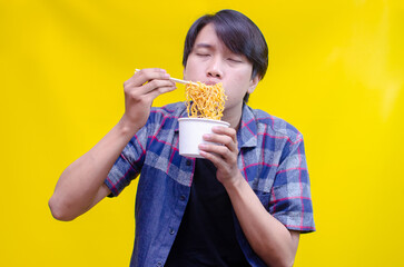 Asian man eats noodles in paper cup hungrily and passionately. Attractive man eats fried instant noodles using chopstick