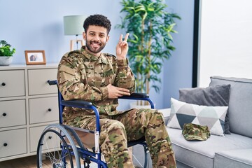 Arab man wearing camouflage army uniform sitting on wheelchair smiling with happy face winking at...