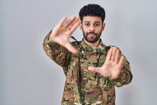 Arab man wearing camouflage army uniform doing frame using hands palms and fingers, camera perspective