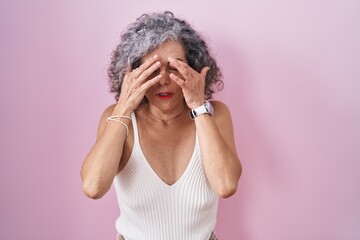 Middle age woman with grey hair standing over pink background rubbing eyes for fatigue and...