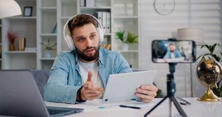 Blogger talk to camera record new educational videovlog on smartphone on tripod in living room....