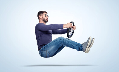 Happy bearded man in glasses drives a car with a steering wheel on light blue background. Auto...