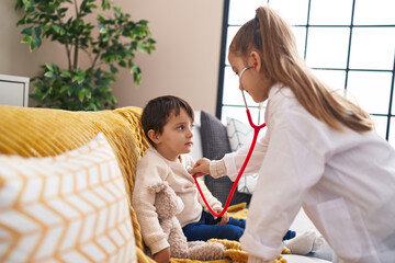 Adorable boy and girl wearing doctor uniform examining with stethoscope at home