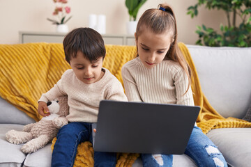 Adorable boy and girl using laptop sitting on sofa at home