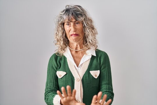 Middle age woman standing over white background disgusted expression, displeased and fearful doing disgust face because aversion reaction.