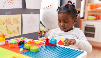 African american girl playing with construction blocks sitting on table at kindergarten