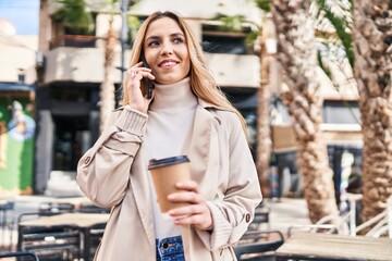 Young blonde woman talking on smartphone drinking coffee at coffee shop terrace