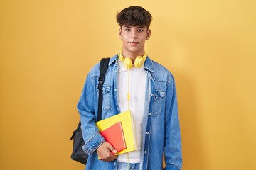 Hispanic teenager wearing student backpack and holding books with a happy and cool smile on face....
