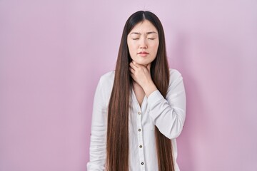 Fototapeta premium Chinese young woman standing over pink background touching painful neck, sore throat for flu, clod and infection