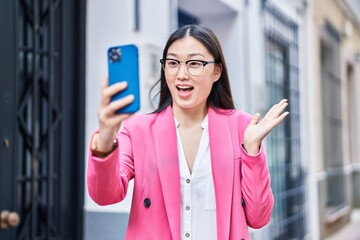 Fototapeta premium Chinese young woman doing video call with smartphone celebrating achievement with happy smile and winner expression with raised hand