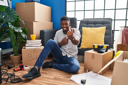 African american man sitting on the floor at new home beckoning come here gesture with hand inviting welcoming happy and smiling