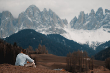 A man sits on a hill in front of a mountain with the mountains in the background. Hiking in the mountains. The alps.