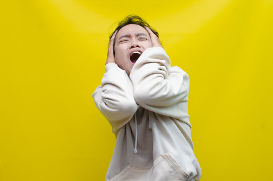 portrait of the anger expression of an Asian young man in beige hoodie, threatening, accusing, and looking for fight. A hysterical, mad depressed indonesian young man hand, shouts and screams loudly.