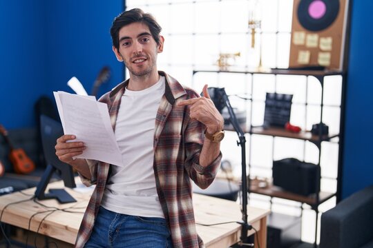 Young hispanic man reading music sheet at music studio pointing finger to one self smiling happy and proud