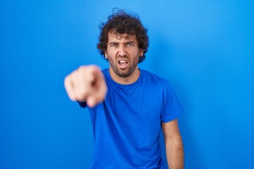 Fototapeta na wymiar Hispanic young man standing over blue background pointing displeased and frustrated to the camera, angry and furious with you