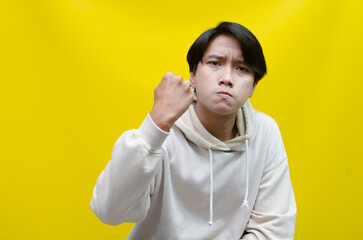 Naklejka premium an Asian young man in beige hoodie, threatening, accusing, and looking for fight. A hysterical, mad depressed indonesian young man hand, shouts and screams loudly.