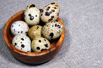 Quail eggs in a round wooden bowl on canvas, close-up, macro. Eggshell stains. Spotted pattern on the eggs. Dietary healthy foods. Egg