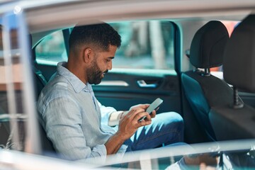 Young arab man using smartphone sitting on car at street