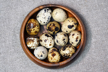 Quail eggs in a round wooden bowl on canvas, close-up, macro. Eggshell stains. Spotted pattern on the eggs. Dietary healthy foods. Egg